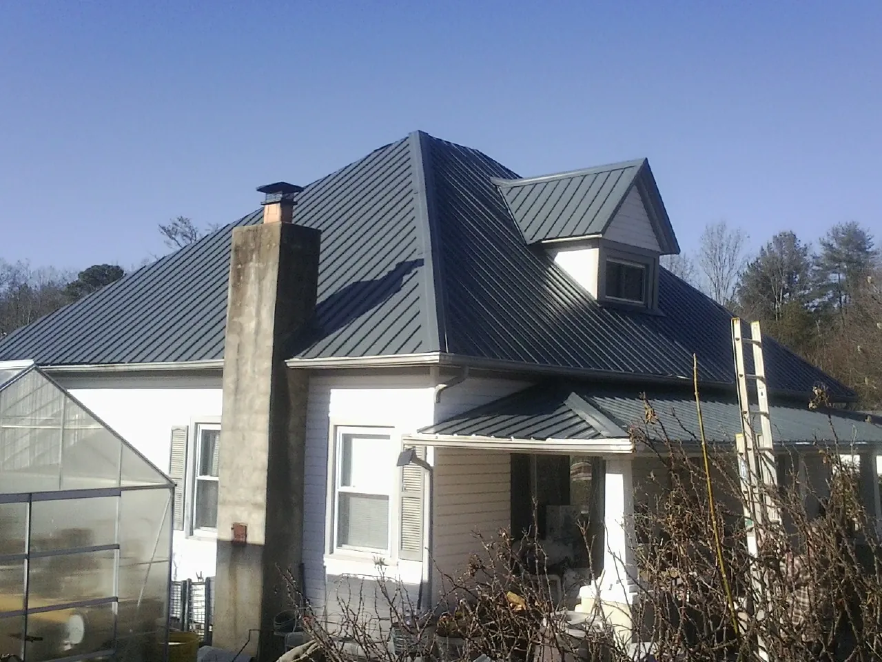 Dark blue standing seam metal roof on a white farmhouse with dormer — Slate & Tile Roof Repair by Roofing Brothers in East Branch