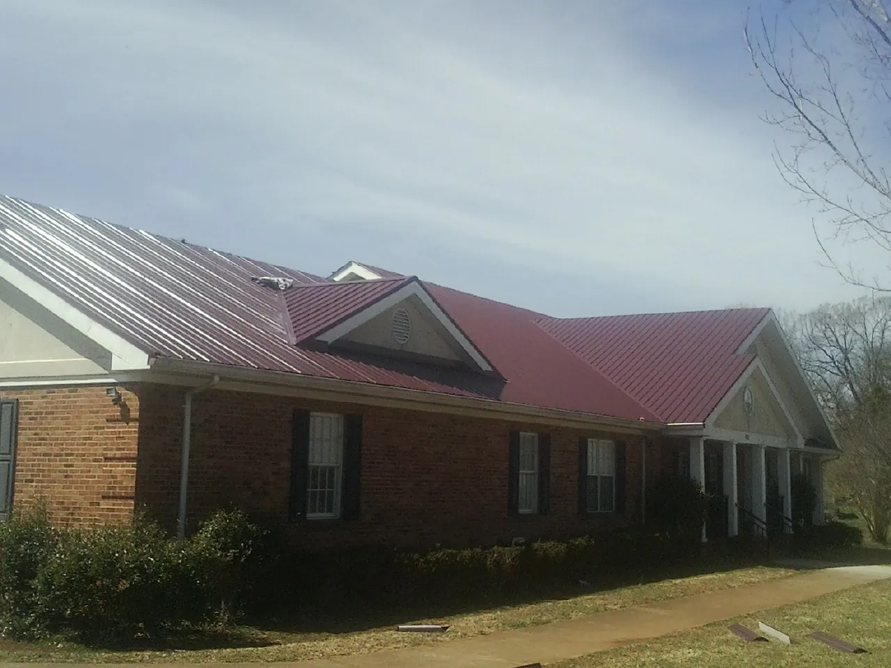 Red metal roof with gabled entries on a long brick building, from a Hail Damage Roof Repair job in East Branch