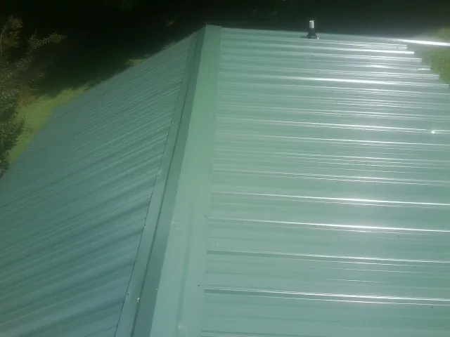 New green metal panels meeting at the ridge of a roof — Flat Roof Repair work by our crew in East Branch