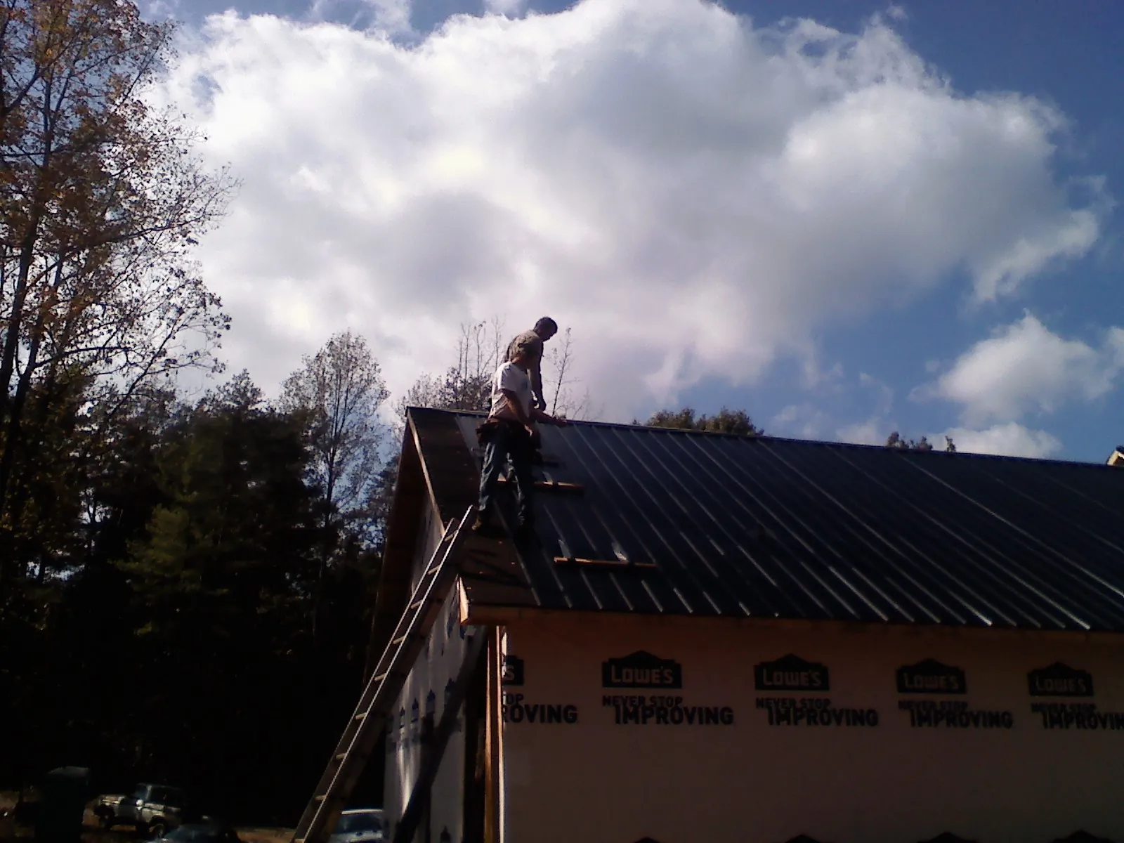 Roofer fastening dark metal panels high against a cloudy sky, from a Roof Inspection job in East Branch