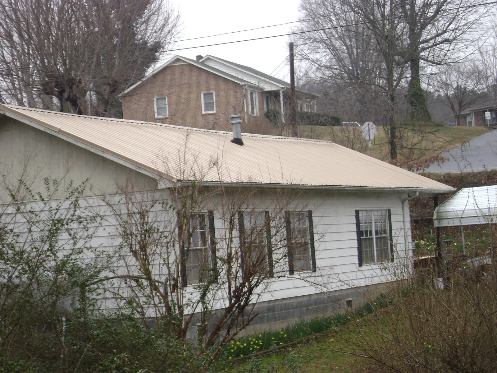 Tan metal roof on a white sided house set into a hillside — Commercial Roofing by Roofing Brothers in East Branch
